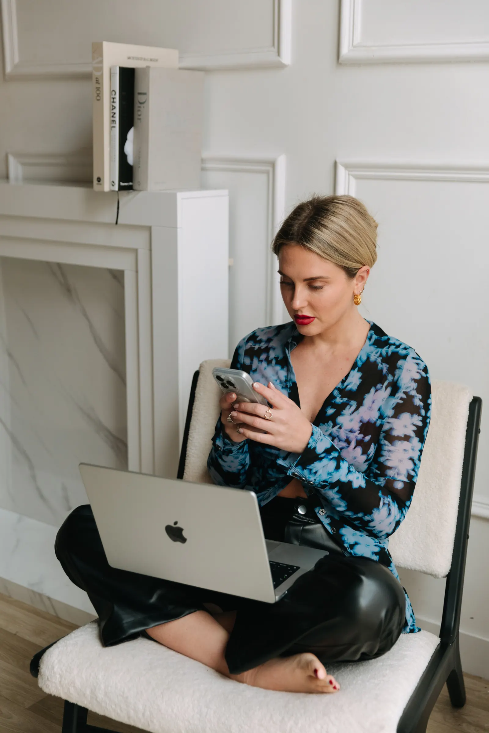 Emily in a blue floral top sitting on an armchair with her laptop and phone