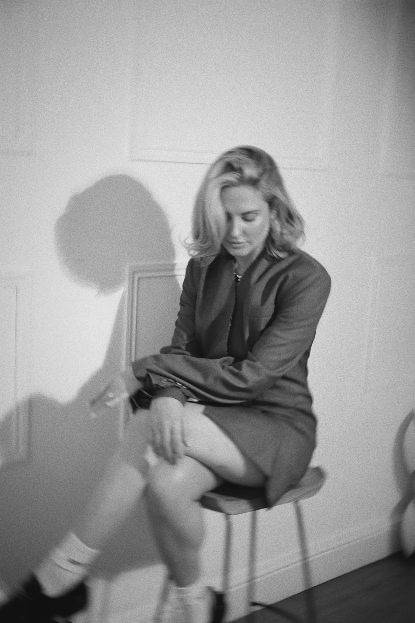 Emily in black and white, seated on a stool in a grey blazer
