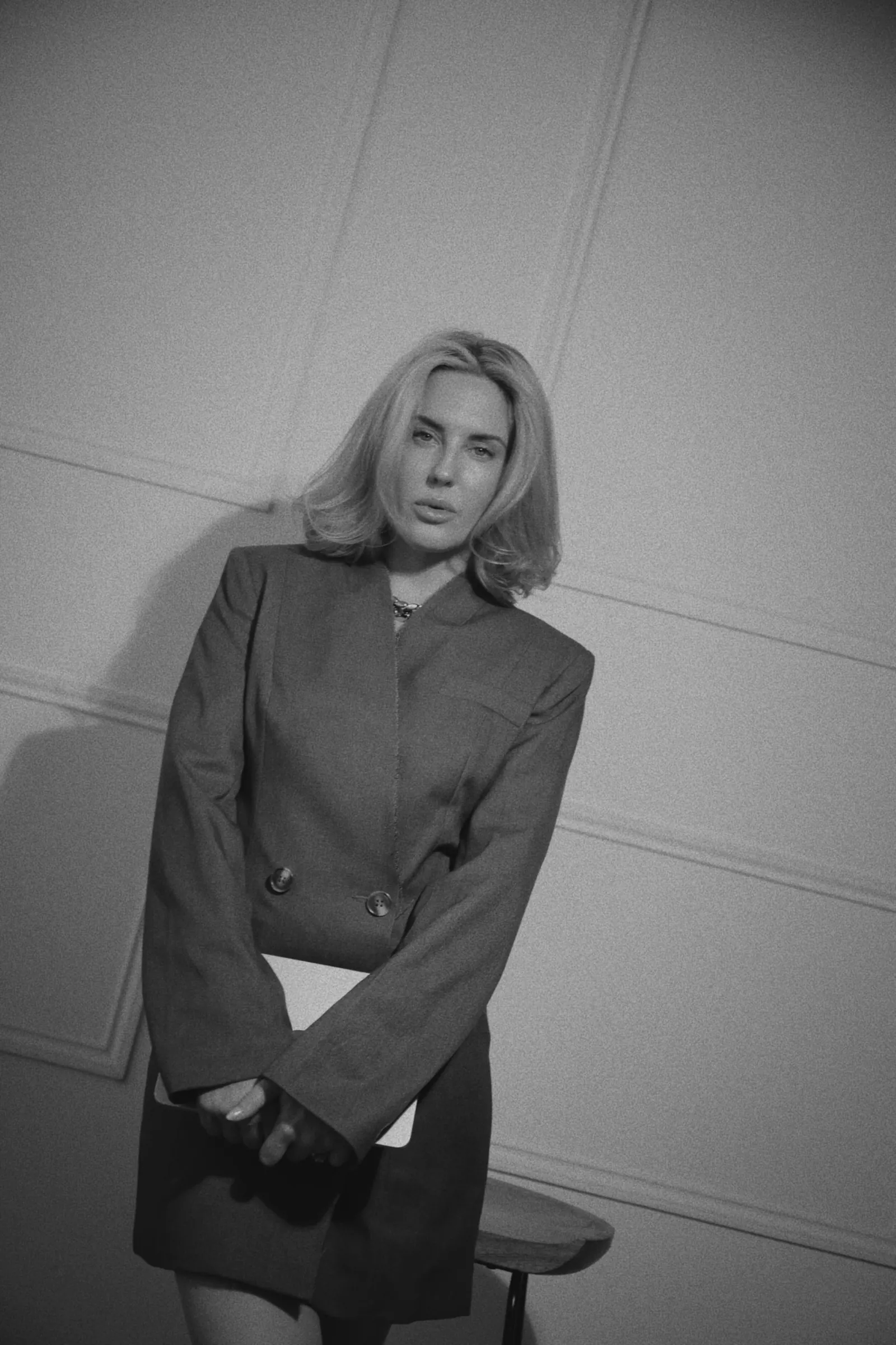 Emily in black and white leaning against a wall in a cropped blazer