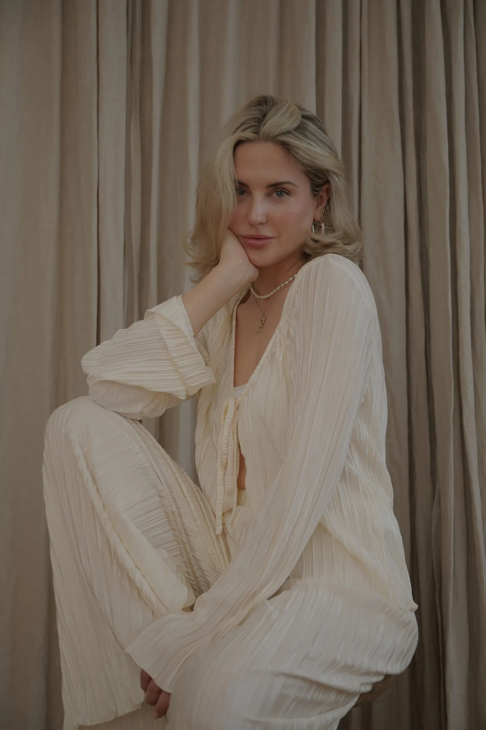 Emily in a cream set posing against a beige curtain