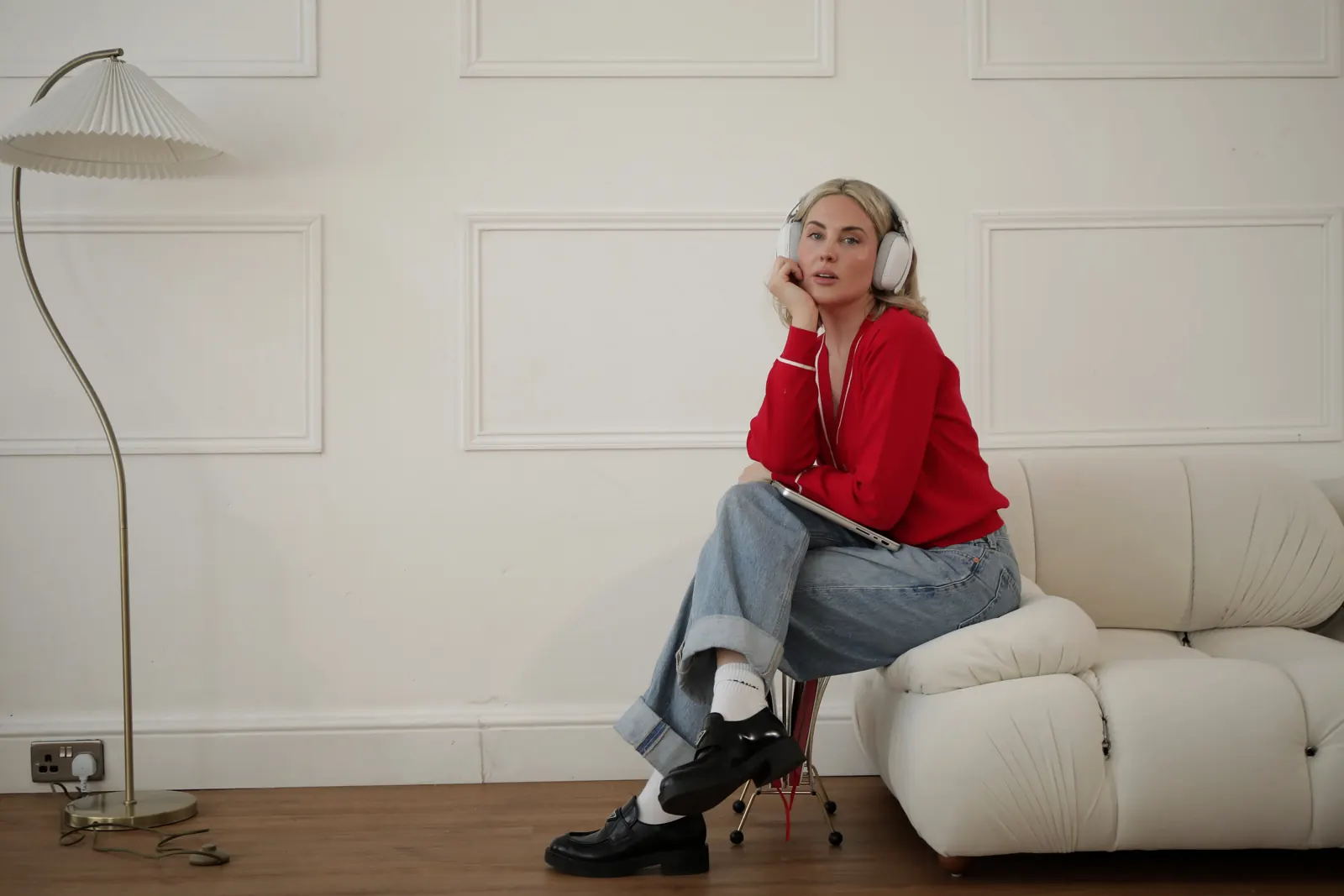 Emily in a red cardigan sitting on a cream chair in jeans and boots